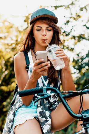 Young urban woman sitting on bicycle and using smart phoneの写真素材