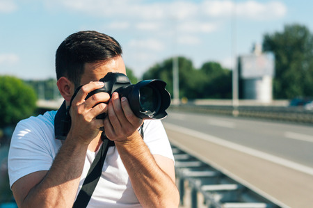 Young man with professional camera photographing outside.の写真素材