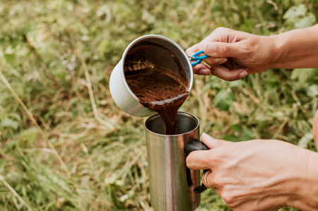 Woman in a pours hot coffee in the cup, outdoors.の写真素材