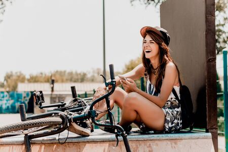 Beautiful young woman sitting next to her bike outdoors, holding phone.の写真素材