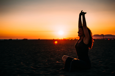 Woman practicing yoga on the beach at sunsetの写真素材