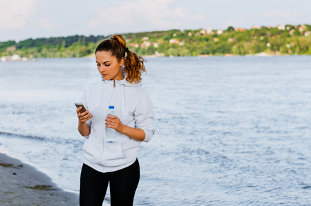 Relaxed fitness woman resting after exercising, using phone.の写真素材