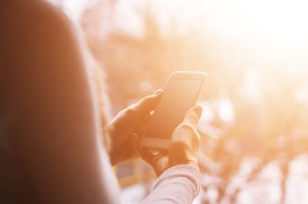 Beautiful young woman's hand using smart phone outside, flare lightの写真素材