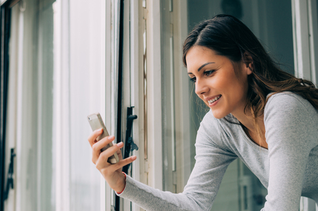 Girl checking mobile at an open windowの写真素材