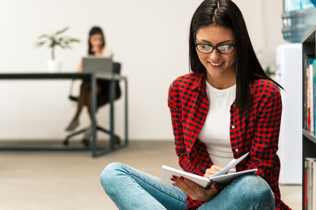 Smiling young woman sitting on floor with book.の写真素材