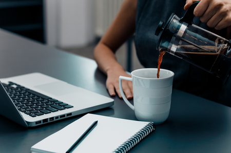 Woman hands pouring coffee into cup on office table.の写真素材