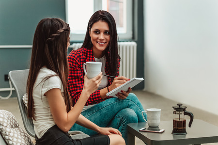 Young businesswomen sitting at office desk, looking at each other and smiling.の写真素材