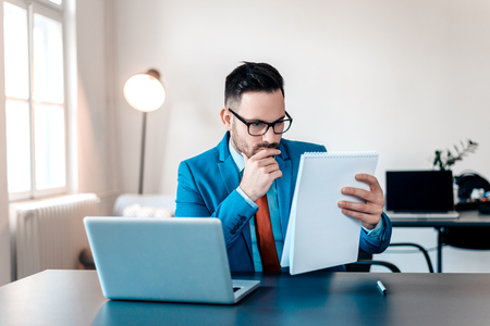 Concentrated young businessman reading documents at office desk.の写真素材