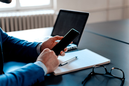 Close up of businessman using mobile phone at office desk.