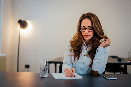 Attractive caucasian woman writing in notepad at workplace.の写真素材