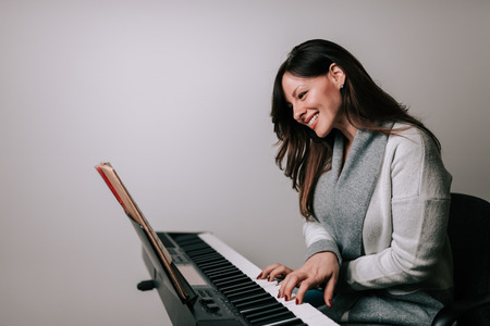 Smiling woman pianist playing synthesizer from sheet music.の写真素材
