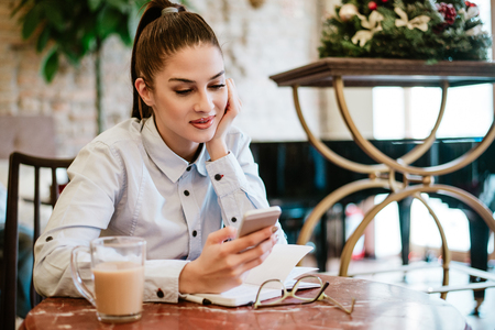 Gorgeous young woman looking at mobile phone while sitting in the cafe.の写真素材