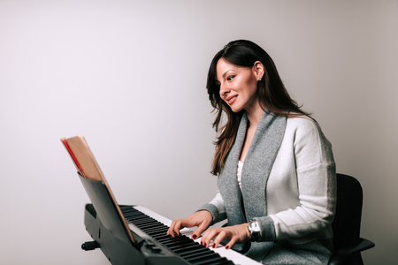 Beautiful woman playing synthesizer from music sheet. Isolated background.の写真素材