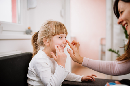 Smiling mother applying creme on her little daughter face.の写真素材