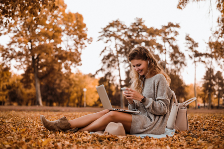 Young fashion blogger woman using phone in park.の写真素材