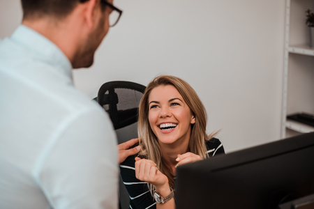 Cheerful young woman in office talking with man.の写真素材