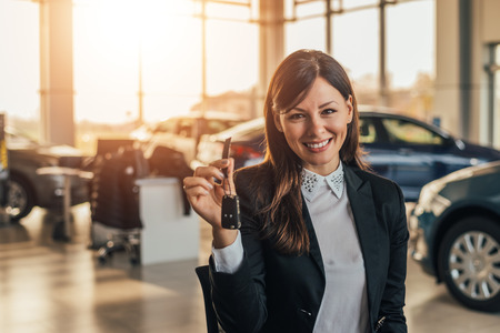 Cheerful young woman showing her new car key at dealership.の写真素材