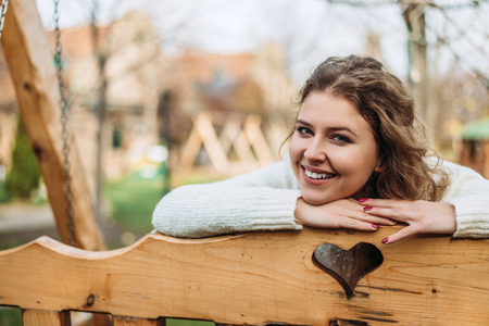 Smiling blonde woman leaning on wooden bench outside.の写真素材