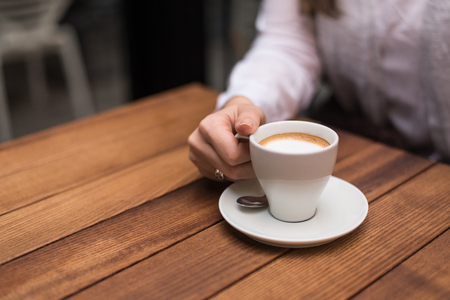 Woman's hand holding coffee cup on wooden table.の写真素材