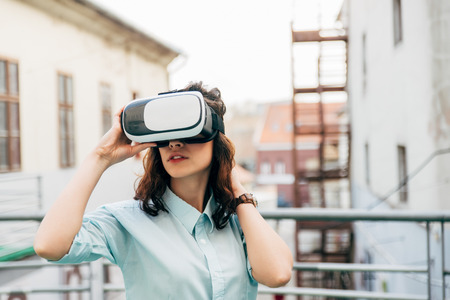 Brunette woman girl with waving hair uses virtual reality glasses in the urban space