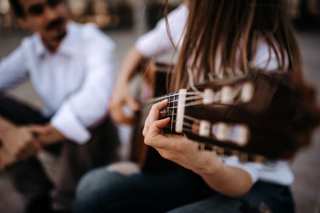 Playing acoustic guitar in the city. Blured image of a girl playing guitar while sitting with male...