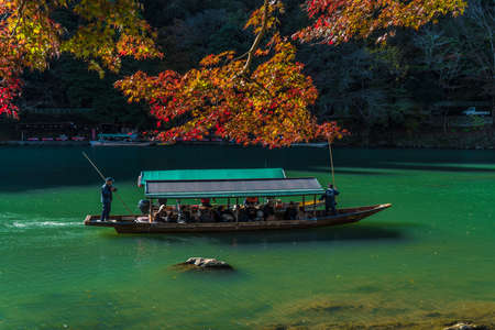 Arashiyama, Japan- Nov 29, 2015 : Group of Tourists cruising with blue jacket Japanese Ferryman in the River at Arashiyama on 29 Nov.のeditorial素材