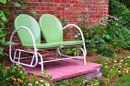 Backyard garden with glider on brick floor, flowers and brick wall in backgroundの写真素材