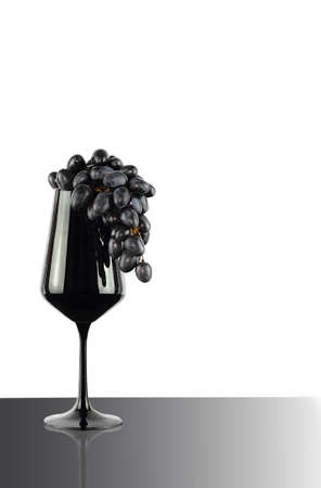 Black drink wine glass with dark blue grapes on white backgroundの写真素材