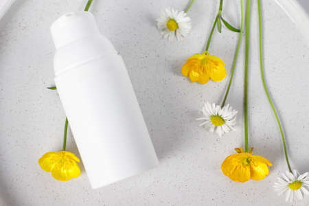 White plastic cosmetic bottle on marble plate, flowers, mockup