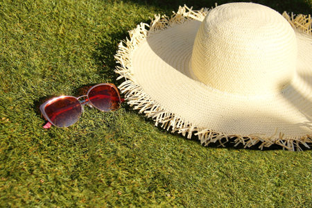 Sunglasses and beige straw hat on green grass, summer tropical dayの写真素材
