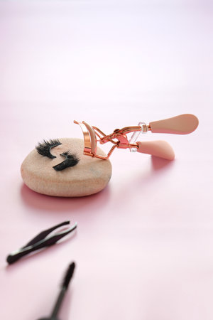 Pink eyelashes curler tool and false eye lashes on colorful background