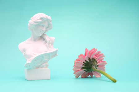 Female face bust statue greek style with pink gerbera flower on blue backgroundの写真素材