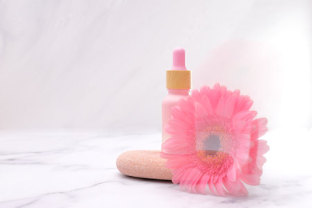 Mockup glass pink bottle of serum with gerbera flower and stoneの写真素材