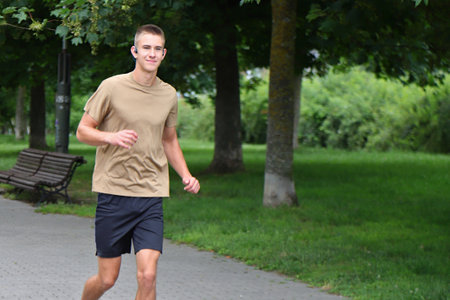 Young man running in urban park, teenager jogging with headphones on street, in motionの写真素材