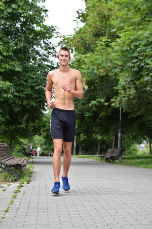 Young man running in urban park, teenager jogging with headphones on street, in motionの写真素材