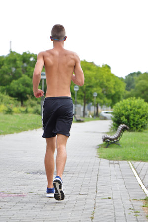 Young man running in urban park, teenager jogging with headphones on street, in motionの写真素材