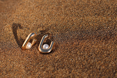 Pearl golden earrings on sand, beach stylish accessories, luxury concept