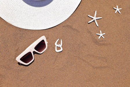 Sunglasses, hat and earrings on sand with shells, beach accessoriesの写真素材