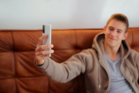 Teenager boy with smartphone, boy looking at device sitting on sofaの写真素材