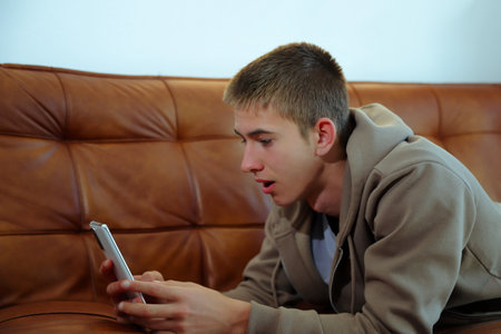 Teenager boy with smartphone, boy looking at device sitting on sofaの写真素材