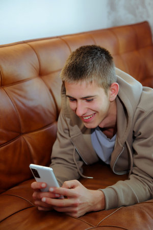 Teenager boy with smartphone, boy looking at device sitting on sofaの写真素材