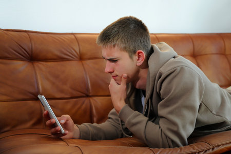 Teenager boy with smartphone, boy looking at device sitting on sofaの写真素材