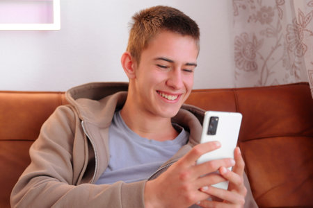 Teenager boy with smartphone, boy looking at device sitting on sofaの写真素材