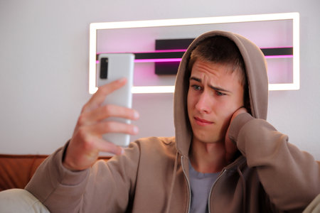 Teenager boy with smartphone, boy looking at device sitting on sofaの写真素材
