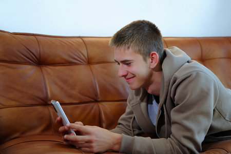 Teenager boy with smartphone, boy looking at device sitting on sofaの写真素材