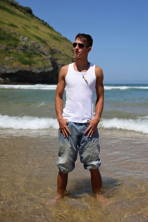 Young caucasian guy in sunglasses on the beach, casual teenager style, summer lifestyleの写真素材