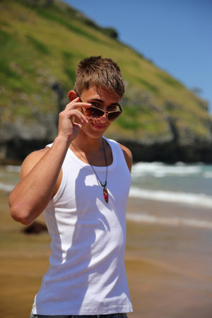 Young caucasian guy in sunglasses on the beach, casual teenager style, summer lifestyleの写真素材