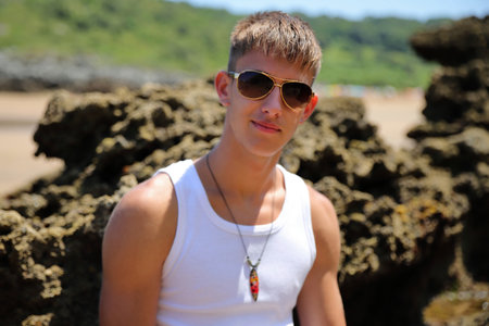 Young caucasian guy in sunglasses on the beach, casual teenager style, summer lifestyleの写真素材