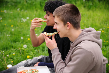 Two friends dining outside, eating pizza in parkの写真素材