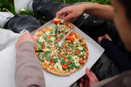 Two friends dining outside, eating pizza in park